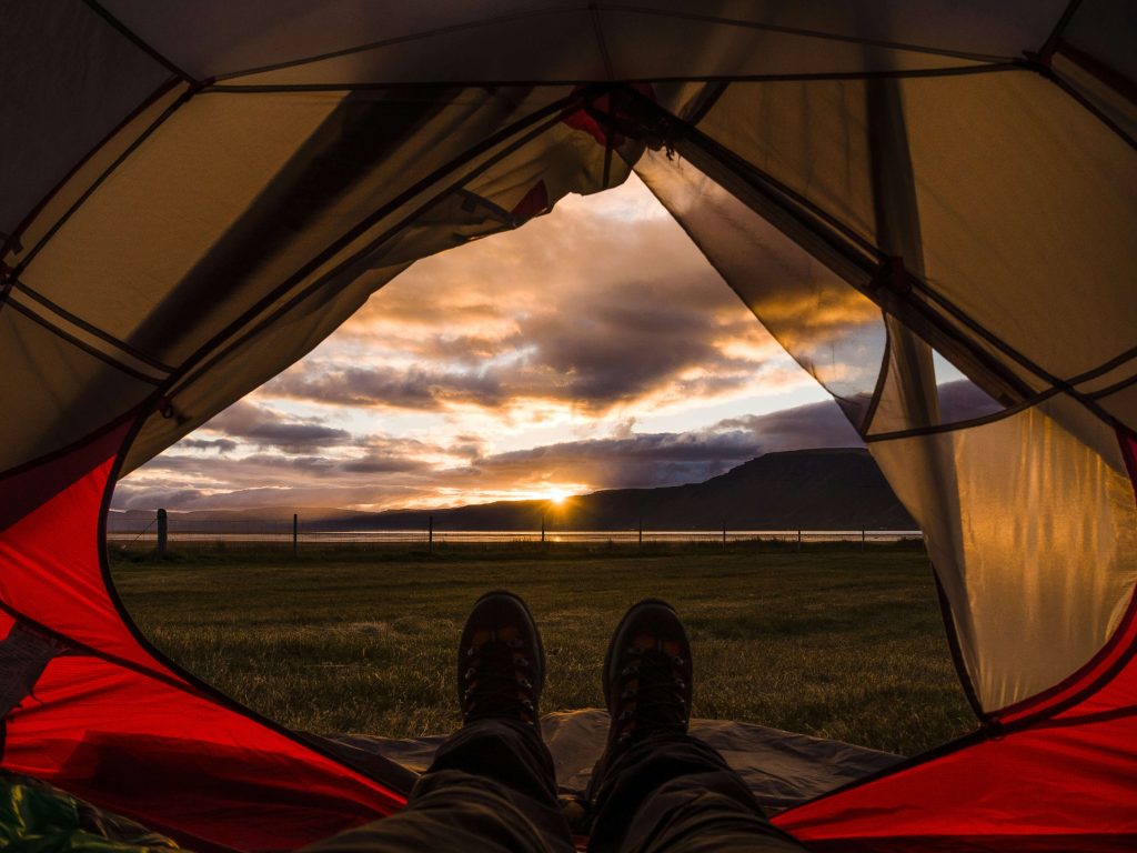 an image showing a partially open tent door looking across a sunset field and sea scene. Shoes and trousers in the centre of the image